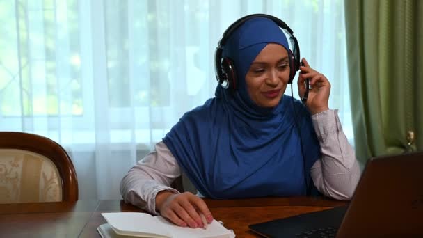 有信心的阿拉伯穆斯林妇女 呼叫中心工作人员 自由职业者 头戴蓝色头巾 头戴音响耳机的企业家 在家里远程办公时通过视频链接与伴侣交谈 非常迷人 — 图库视频影像