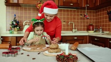 Anne ve kızı rulo zencefilli ekmek hamurundan şekiller keserken, aynı zamanda sıcak, sade bir ahşap mutfakta şenlikli hamur işlerinin tadını çıkarıyorlar. Mutlu Noeller ve iyi tatiller.