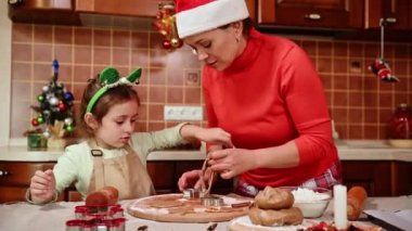 Mutlu noeller. - Mutlu yıllar. Zencefilli çörek. Pişirme. Anne ve kızını sevmek, kurabiye yapmak, farklı şekillerde kurabiyeler kesmek, sade mutfakta tahta kalıpta metal kalıplar kullanmak.