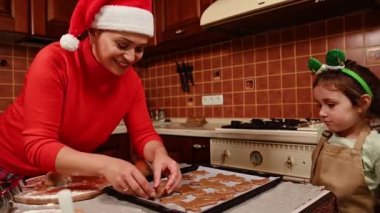 Çok ırklı güzel bir kadın, Noel Baba şapkalı sevgi dolu bir anne, hamur yoğurma, tatlı kızıyla zencefilli kurabiye pişirme. Mutlu noeller. Aile gelenekleri. Annemle yemek pişirmenin mutluluğu.
