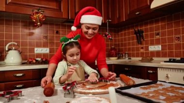 Kızıyla genç ve çekici bir kadının Noel tatili için zencefilli kurabiyeler hazırladığı bir fotoğraf. Sevimli kız annesine Noel kurabiyeleri pişirmesinde yardım eder. Aile tatillerini birlikte geçirme kavramı