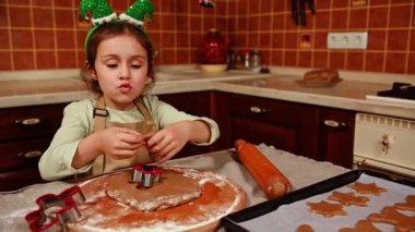 Güzel beyaz bir çocuk, şirin bir kız elf halkası takıyor ve bej şefler önlük takıyor zencefilli ekmek hamurundan şekiller kesiyor, Noel tatili için pasta pişirmekten zevk alıyor. Mutlu çocukluk