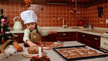 Beyaz aşçı şapkası ve bej önlük takan yaramaz, sevimli bir fırıncı kız. Mutfak adasında duruyor. Noel için zencefilli kurabiye pişirmekten hoşlanıyor.