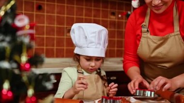 Küçük tatlı kız şekerlemecinin Noel arifesinde Noel kurabiyesi pişirmesini öğrendiği 4K video kaydı. Sevgi dolu anne kızına zencefilli tatlı yapmayı öğretir. - Aile. Noel yemeği konsepti.