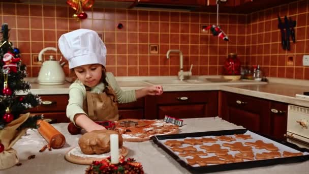 迷人的白种人小女孩 一个头戴白厨师帽 头戴米黄色围裙 淘气的可爱儿童面包师 站在厨房的小岛上 她喜欢为圣诞节做姜饼 — 图库视频影像