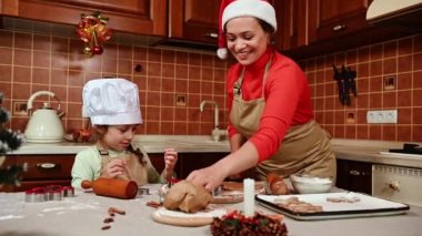 Mutlu bir aile, Noel Baba şapkalı sevgi dolu bir anne ve sevimli küçük kızı, ikisi de şeflerin önlüklerinde, birlikte eğleniyorlar, şirin bir Noel arifesinde şenlikli pastalar pişiriyorlar. İyi tatiller.