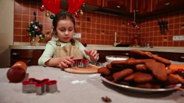 Geyik boynuzu halkası takan, mutfak masasının başında dikilen, zencefilli ekmek hamurundan şekiller kesen ve Noel hediyesi alırken aniden sevinen beyaz bir kız.