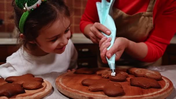 愛らしい白人の子供 白いセーターの少女と11のフープは ジンジャーブレッドクッキーを見て 彼女の母親はアイシングでそれらを飾ります 焼き釉薬でケーキを飾る クリスマスベーカリー — ストック動画