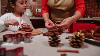 Geyik boynuzu halkası takan, elinde zencefilli ekmek tutan ve keten iple zencefilli kurabiye bağlayıp hediye kutusuna koyan annesine bakan sevimli beyaz kız. Noel
