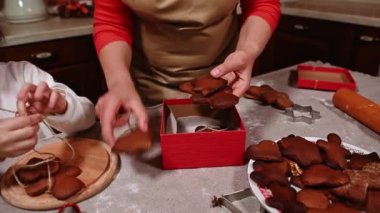 Bir kadın, anne ve kızı ev yapımı zencefilli kurabiyeleri keten iple bağlayıp şirin bir Noel arifesinde kırmızı hediye kutusuna diziyorlar. Mutfak. Şenlikli fırın. Şekerlemeci