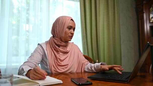 工作负担过重 任务繁多 头戴头巾的阿拉伯穆斯林妇女感到困惑 在笔记本上记笔记 在笔记本电脑显示器上打字 在失败的项目中感受到压力 电子通勤 商业失败 — 图库视频影像