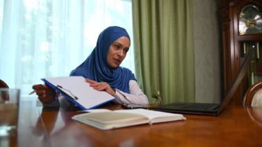 Orta Doğu 'nun güzel, başarılı kadını, mavi başörtüsü takıyor, müşterilerle veya iş ortaklarıyla telekomünikasyon yaparken video konferansı yaparken panoda şemalar gösteriyor, dizüstü bilgisayar kullanıyor.