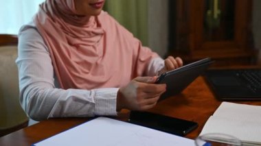 Arap Müslüman kadınların elleri dijital tablet kullanır, haber kaynaklarını kaydırır, sağa sola kaydırır, web sitelerine göz atar ve internette sörf yapar, lüks ofis içinde ahşap bir masada otururken