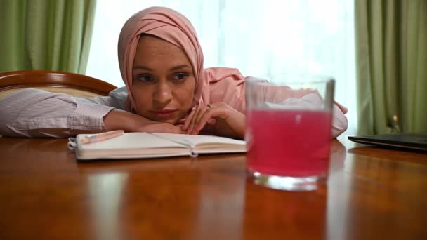 ピンクのヒジャーブの美しい中東イスラム教徒の女性 木製のテーブルに対して彼女の頭を傾けます 頭痛を感じます 水のガラスの中に発酵タブレットを溶解見ながら疲れと燃え尽きて感じます — ストック動画