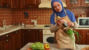 Büyüleyici ev hanımı, Arap Müslüman kadın marketten sonra taze organik sebzeler ve meyvelerle dolu bir poşet açıyor. Mutlu Orta Doğulu ev hanımı, evin mutfağında duruyor.