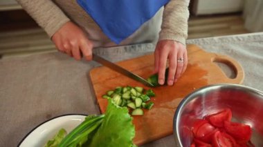 Yakın plan. Kadın elleri mutfak bıçağı kullanıyor, olgun organik salatalıkları tahta kesme tahtasıyla dilimliyor. Mutfakta salata için sebze kesen bir şefin elleri. Sağlıklı çiğ vejetaryen yemeği