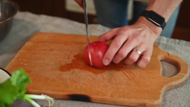 接近中だ 木製のまな板に新鮮な熟した有機ジューシーなトマトをスライス キッチンナイフを使用して男性の手 キッチンでサラダ用の野菜を切るシェフの手 ヘルシーな生ビーガンフード — ストック動画