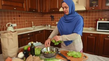 Orta Doğulu, mavi tesettürlü, taze salata yaprakları kesen, evdeki mutfakta çiğ vegan sağlıklı salata hazırlayan çekici bir Müslüman kadın. Diyet yapıyorum. Sağlıklı beslenme. Kilo kaybı ve zayıflama kavramı.