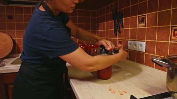 缶入りのゆでたトマトジュースやパスタで瓶の蓋を閉めた主婦の横の肖像画 缶詰だ 引っ張れ 自家製の缶詰を調理する 海洋生物 — ストック動画