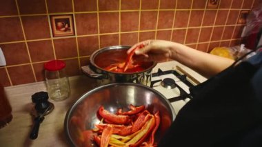 Siyah şef önlüklü bir ev kadınının arka görüntüsü, haşlanmış domates suyuyla dilimlenmiş dolma biber koyması, organik sulu domates ve biber salatası hazırlaması, kış için sebze konservesi.