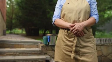 Steadicam shot: Mavi gömlekli ve bej önlüklü güzel Afro-Amerikan kadın portresi, başarılı amatör çiftçi, bahçıvan, organik bir çiftlikte bahçıvan, kameraya gülümseyen dişli gülümseme