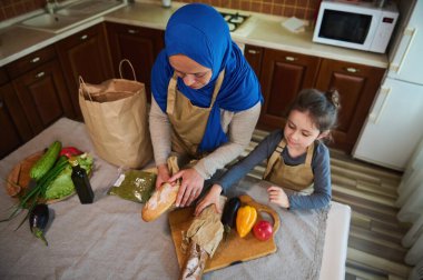 Üst Manzara. Mutlu Orta Doğulu aile ilişkileri. Arap Müslüman bir kadın, kızını seven bir anne yiyecek, sebze ve meyve paketleri hazırlamak için marketten birlikte geliyor.