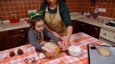Üst Manzara. Güzel bir kadın, sevgi dolu bir anne ve kızı, her ikisi de bej rengi önlüklü, hamuru oklavayla yoğurup yuvarlıyor, ev mutfağında bir Noel tatlısı hazırlıyorlar.