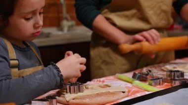 Beyaz önlüklü sevimli beyaz kız zencefilli kurabiye hamurundan bir kar tanesi şeklini kesip kameraya gösteriyor ve Noel için ev yapımı lezzetli kurabiyeler yapıyor..