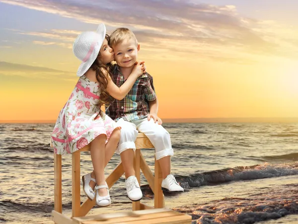 Little girl kissing boy on sea landscape at sunset — Stock Photo, Image