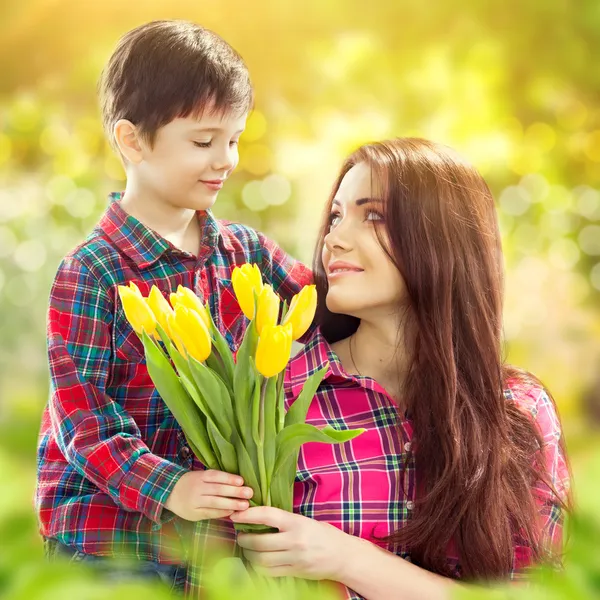 Sønnen klemmer moren sin og gir henne blomster – stockfoto