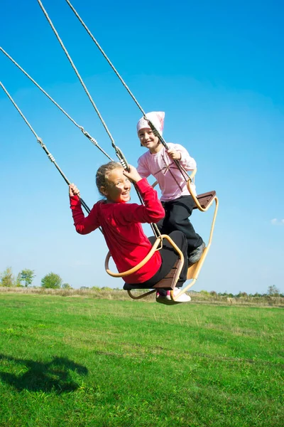 Two Happy Girls Sitting Swing Having Great Fun Playground Park — стоковое фото