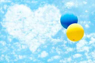 Mavi gökyüzünde mavi ve sarı renkli Ukrayna bayraklı iki balon ve kalp şeklinde bulutlar..