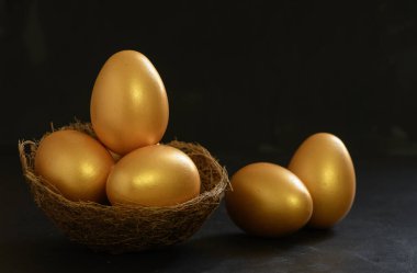 Yuva kuşunda ve siyah masa arkasında altın paskalya yumurtaları.