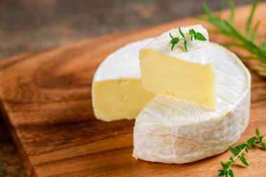 Tahta tabakta kekik ile dilimlenmiş Camembert peyniri. Camembert nemli, yumuşak, kremalı, yüzeyde olgunlaşmış inek sütü peyniri..