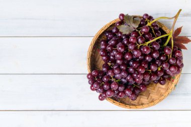 Şampanya üzümleri bambu sepetinde ve beyaz ahşap arka planda. Şampanya üzümleri çok küçüktür ve sıkıca paketlenmiş kümelerde yetişir. Çekirdeksiz böğürtlenler koyu kırmızı, meyve konsepti.