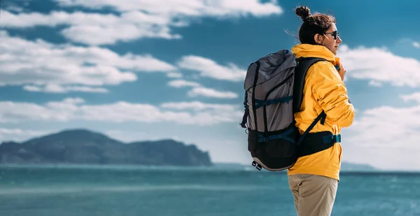 パノラマに対するバックパックで観光客 空に対する観光ギアの女性の肖像画 旅行やアクティブなライフスタイルの概念 黄色のジャケットの旅行者の肖像画 スペースのコピー — ストック写真