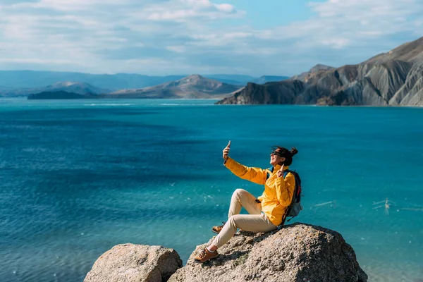 旅人は海を背景に携帯電話で自撮りをする 海岸沿いの旅行者 少女は美しい海を背景に手に携帯電話を持っている スペースのコピー — ストック写真