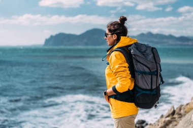 Denizin arka planında sırt çantası olan bir kadın. Denizin arka planında turist kıyafeti giymiş bir kadının portresi. Seyahat konsepti ve aktif yaşam tarzı. Deniz kıyısında bir turist kız.
