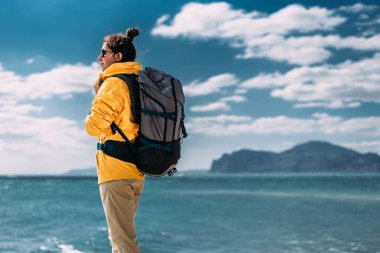 Denizin arka planında sırt çantası olan bir kadın. Denizin arka planında turist kıyafeti giymiş bir kadının portresi. Seyahat konsepti ve aktif yaşam tarzı. Deniz kıyısında bir turist kız.