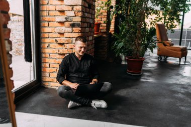 Bir adam kucağında dizüstü bilgisayarla yerde oturuyor. Yerde oturan bir adam dizüstü bilgisayarla çalışıyor. Uzaktan kumanda. Dizüstü bilgisayarı olan başarılı bir genç. Evden çalışan genç bir serbest yazar. Boşluğu kopyala