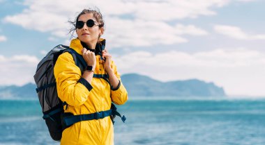 Denizin arka planında bir kadın gezginin portresi. Macera, seyahat ve yürüyüş konsepti. Bir dişi turist yürüyüş sırasında güzel bir manzaranın tadını çıkarır. Deniz kenarında bir turistin portresi