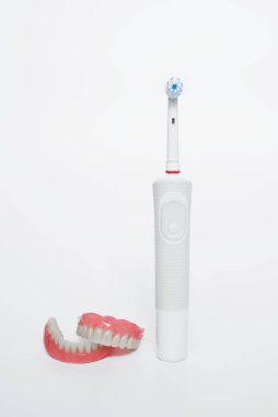 Elektrikli fırçayla diş bakımı. Takma dişler ve beyaz arka planda elektrikli fırça. Akrilik protezler. Ağız temizliği. Ortopedik dişçilik. Takma diş. Açık arkaplanda diş ve diş fırçası