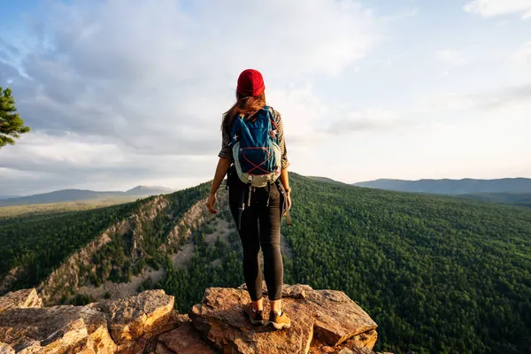 バックパック付きの若い女性観光客は山の頂上からの夕日を賞賛します 山の背景に旅行者 日没時に山の背景に旅行者 スペースのコピー — ストック写真