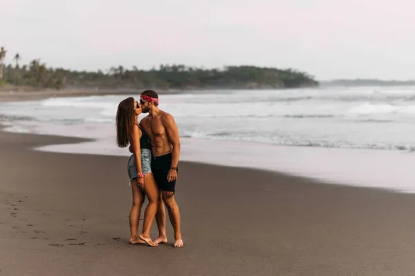 海岸でキスをする美しいカップル バリ島の海岸で恋をしているカップル 浜辺の夕日にキスをする男と女 砂浜でキスをする夫婦を日焼けさせた スペースのコピー — ストック写真