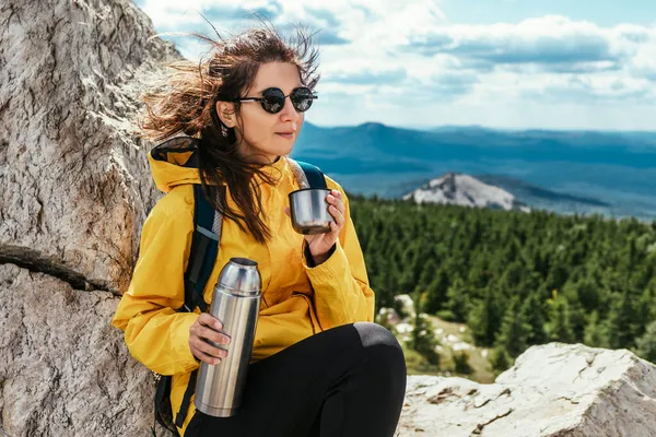 Dişi bir turist dağa tırmandıktan sonra dinleniyor. Bir dişi turist yürüyüş sırasında güzel bir manzaranın tadını çıkarır. Dağların arka planında bir gezginin portresi. Seyahat ve yürüyüş.