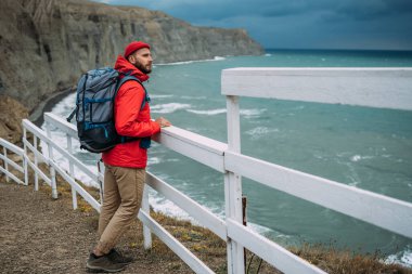 Denizin arka planında sırt çantası olan bir adam. Denizin arka planında turist kıyafeti giymiş bir adamın portresi. Seyahat konsepti ve aktif yaşam tarzı. Deniz kıyısında bir erkek turist