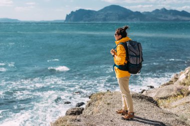Arka planda deniz manzaralı sırt çantalı bir gezgin. Mavi denizin arka planında bir kadın gezgin, panorama. Deniz kıyısında yalnız bir gezgin. Turist bayrağı. Boşluğu kopyala