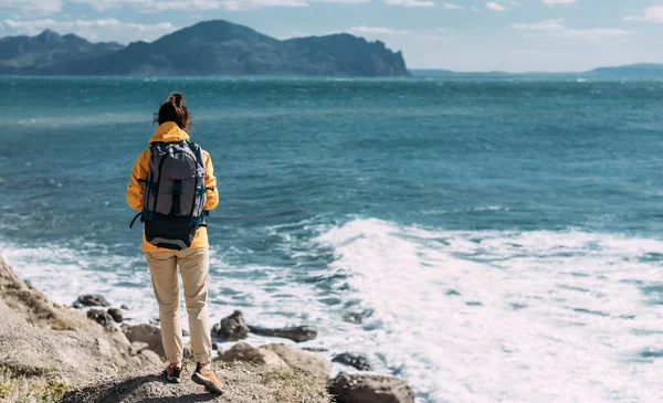 パノラマに対するバックパックで観光客 海に対する観光ギアの女性の肖像画 旅行やアクティブなライフスタイルの概念 黄色のジャケットの旅行者の肖像画 スペースのコピー — ストック写真