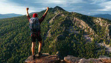 Dağların arka planında sırt çantası olan yalnız bir gezgin, panorama. Dağlarda bir erkek gezgin. Dağın arka planında, dikiz manzaralı, turist kıyafeti giymiş bir adam. Dağlarda yürüyüş.