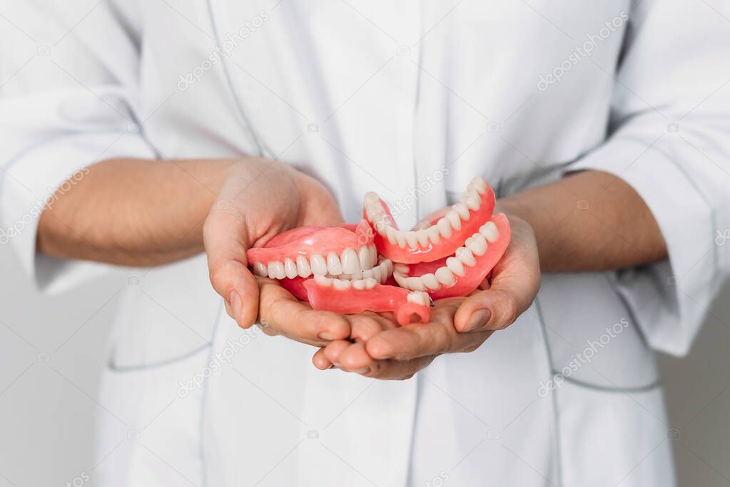An orthopedic dentist holds dentures in his hands. Dentures in the hands of a doctor. Orthopedic dentistry. False teeth. Dentistry conceptual photo. A large number of dentures in the hands of a doctor